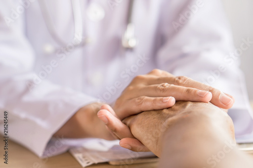 doctor holding hand and comforting old patient in a hospital during their appointment 