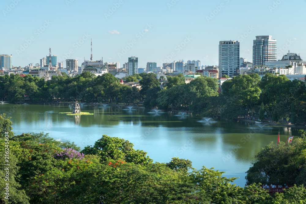 Hoan Kiem lake or Sword lake, Ho Guom in Hanoi, Vietnam with Turtle Tower, green trees and buildings on horizon