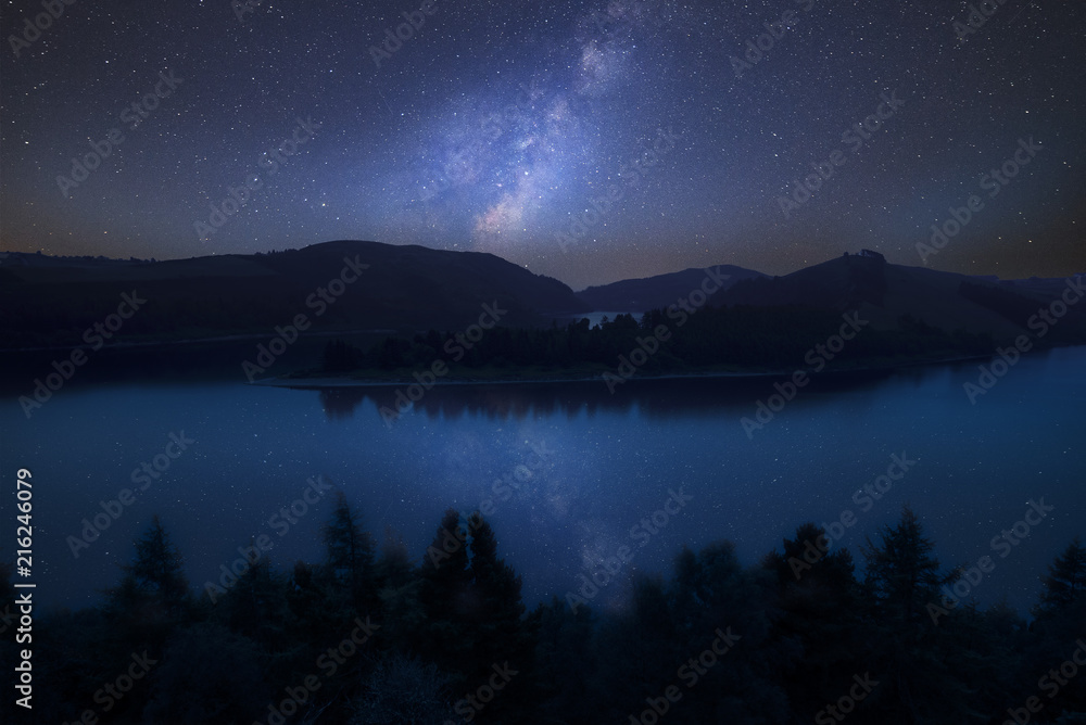 Vibrant Milky Way composite image over landscape of moody still lake