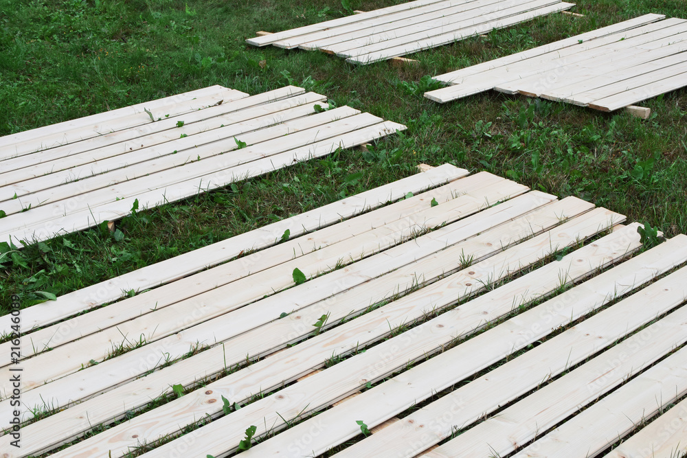 Light natural wooden planks laying on green field grass ready for painting in sunny summer day. Light natural wooden planks laying on green field grass ready for painting in sunny summer day.