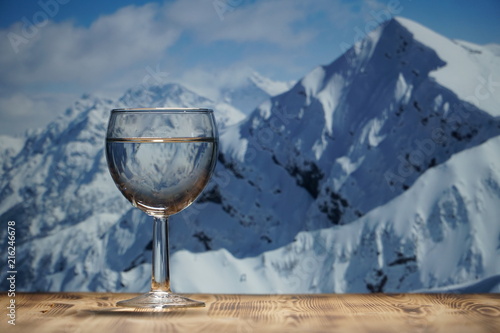 A glass of clean water stands on a wooden table against the winter mountain landscape.