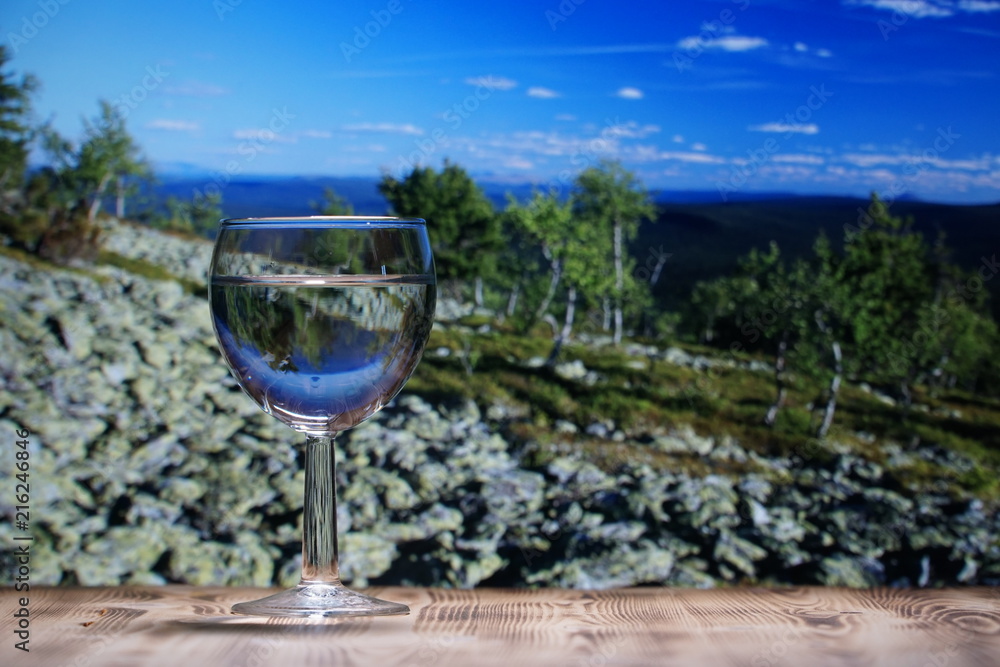 A glass glass glass with clean water stands on a wooden table against a mountain landscape. A glass glass glass with clean water stands on a wooden table against a mountain landscape.