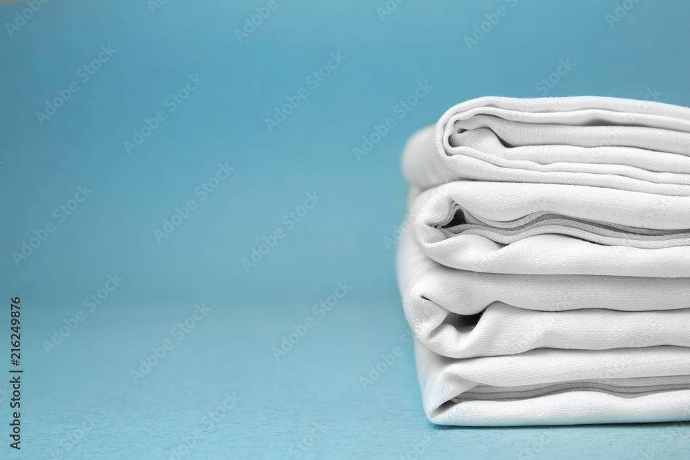 Stack of clean bed sheets on color background - obrazy, fototapety, plakaty 