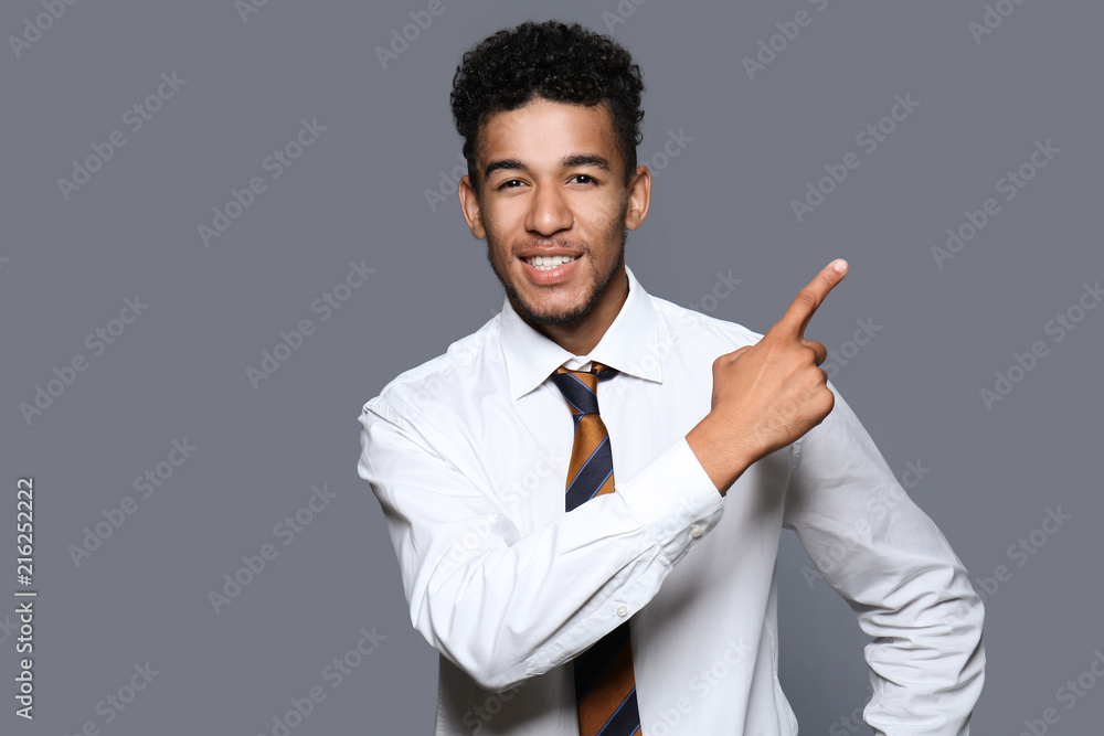 Handsome African-American businessman pointing at something on grey background Handsome African-American businessman pointing at something on grey background