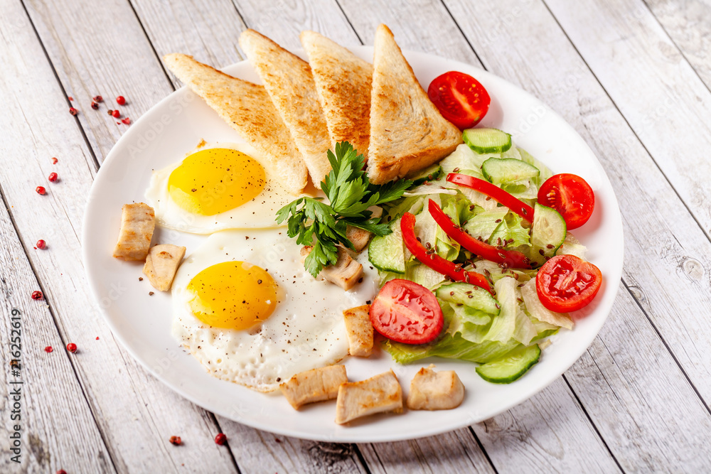 English cuisine, breakfast on a white plate of fried eggs, vegetables and salad with chicken, fried bread toast. Copy space, selective focus English cuisine, breakfast on a white plate of fried eggs, vegetables and salad with chicken, fried bread toast. Copy space, selective focus