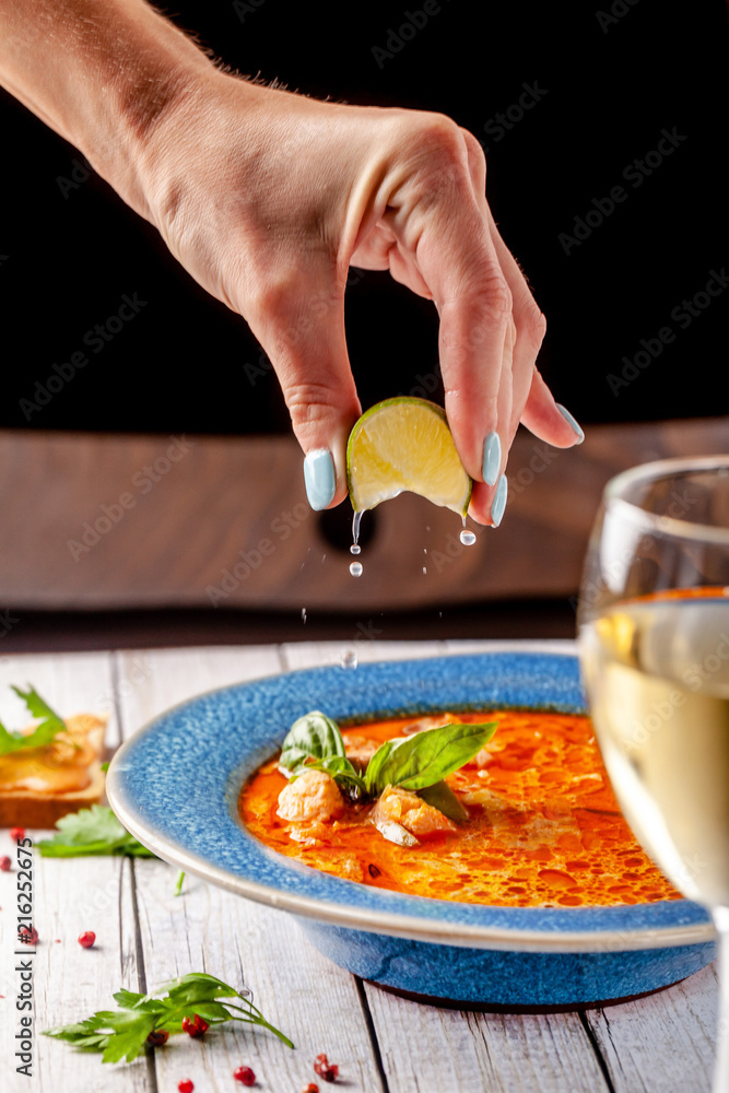 Italian Cuisine. The girl at the restaurant eats fish soup from seafood and salmon, squeezes lime into the soup and drinks white wine. Copy space, selective focus Italian Cuisine. The girl at the restaurant eats fish soup from seafood and salmon, squeezes lime into the soup and drinks white wine. Copy space, selective focus