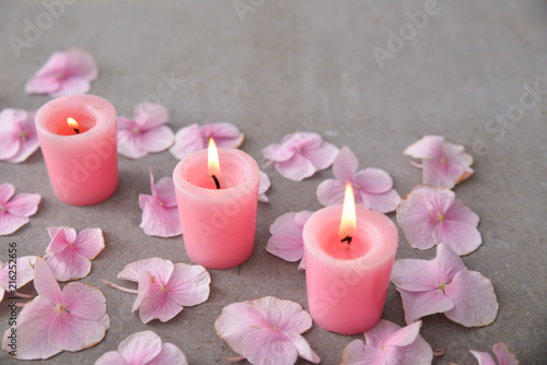Many Pink hydrangea petals with three candle on gray background