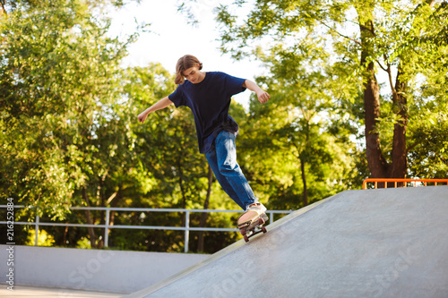 Young guy in T-shirt skateboarding and practicing stunts while spending time in modern skatepark with beautiful view on background
