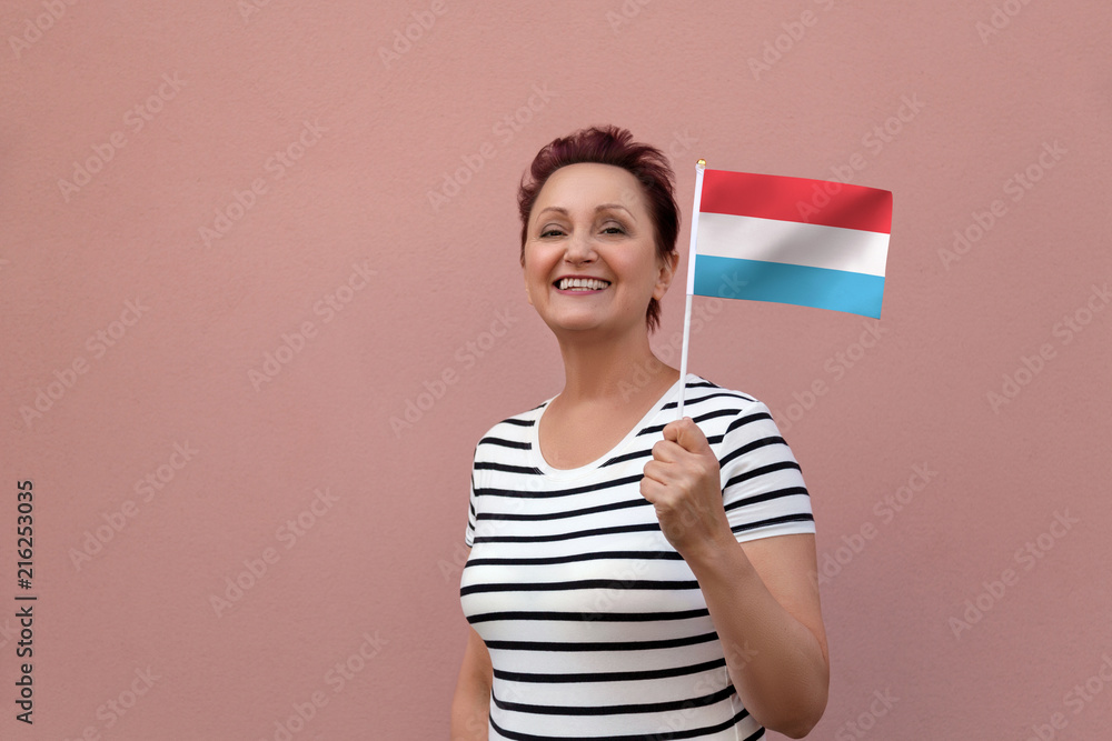 Luxembourg flag. Woman holding Luxembourg flag. Nice portrait of middle aged lady 40 50 years old with a national flag over pink wall background. Luxembourg flag. Woman holding Luxembourg flag. Nice portrait of middle aged lady 40 50 years old with a national flag over pink wall background.