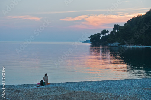 Girl sitting on a beach after sunset, Panormos bay at Skopelos island, Greece