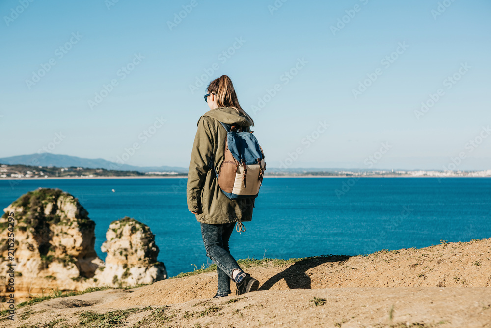A girl tourist or traveler with a backpack walks along the rocky coast and admires the beautiful view of the Atlantic Ocean in Portugal A girl tourist or traveler with a backpack walks along the rocky coast and admires the beautiful view of the Atlantic Ocean in Portugal