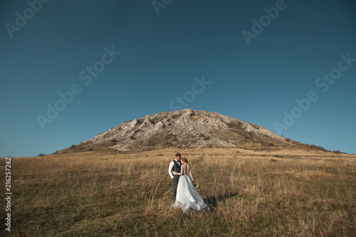 beautiful young couple man and woman standing against the background of a mountain and blue sky in wedding dresses in summer at sunset