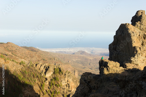 Lonely man sitting on mountain cliff edge in Pico de las Nieves, Gran Canaria. Fearless climber enjoying great views on sunny day in Canary Islands, Spain. Dare, brave, courage concepts