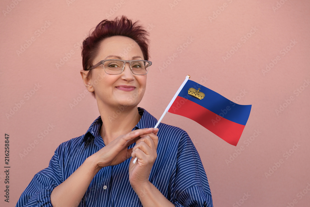 Woman holding flag of Liechtenstein. Nice portrait of middle aged lady 40 50 years old with a national Liechtenstein flag over pink wall background. Visit Liechtenstein concept. Woman holding flag of Liechtenstein. Nice portrait of middle aged lady 40 50 years old with a national Liechtenstein flag over pink wall background. Visit Liechtenstein concept.