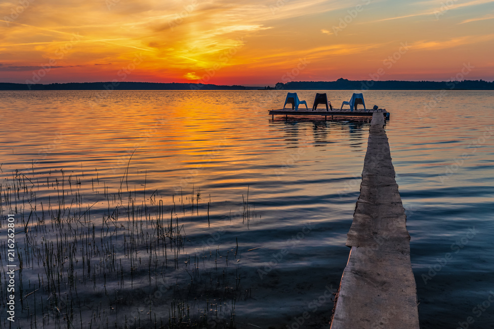 Fototapeta premium Three empty chairs on wooden jetty on lake, during sunrise.