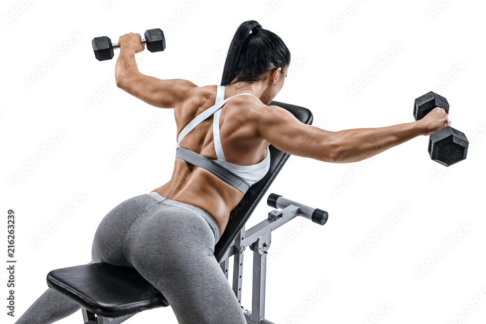 Fototapeta premium Muscular woman doing exercise with dumbbells for muscles of back. Photo of latin woman with good physique lying on sports bench isolated on white background. Strength and motivation