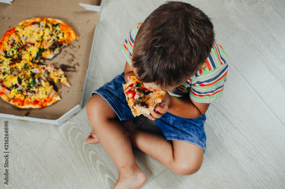 charming boy sitting on the floor eating pizza charming boy sitting on the floor eating pizza