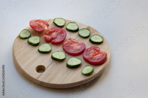 Fresh tomato and cucumber slices on round wooden cutting board