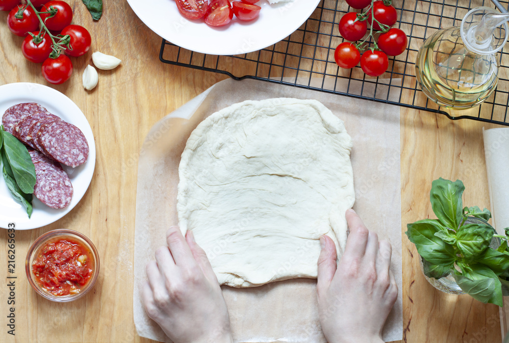 Fototapeta premium Pizza preparation on the wooden table. Food top view. Woman is making dough flat lay