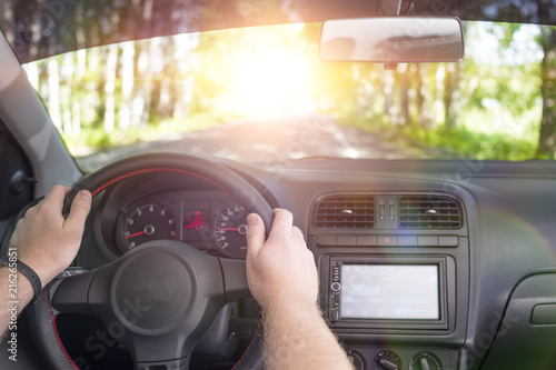 Fototapeta Naklejka Na Ścianę i Meble -  Man in car, hands on steering wheel, road on sunset background. Ciose-up.