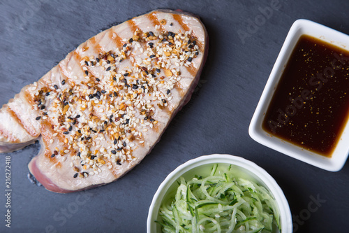 Grilled tuna with sesame and cucumber salad on a black board. Close-up, selective focus.