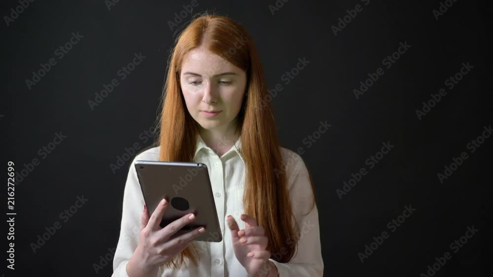 Young ginger woman in white shirt holding tablet with chroma key and showing thumbs up, isolated on black background Young ginger woman in white shirt holding tablet with chroma key and showing thumbs up, isolated on black background