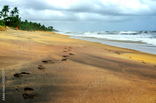 Lonely footprints on a deserted beach in Sri Lanka. Above the stormy ocean, a gloomy cloudy sky with heavy clouds. 