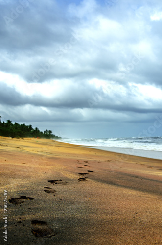 Footprints on a deserted beach in Sri Lanka. Above the stormy ocean, a gloomy cloudy sky with heavy clouds. 