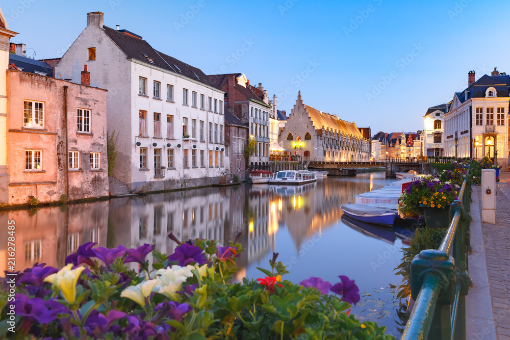 Nice view of picturesque medieval houses on the quay of Leie river and flowers during evening blue hour, Old Town of Ghent, Belgium