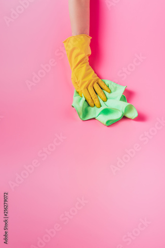partial view of female cleaner wiping dust by rag, pink background