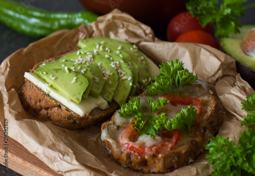 Useful delicious sandwiches - whole wheat bread, tomatoes, avocado and cheese on a paper background. Vegetarian food.
