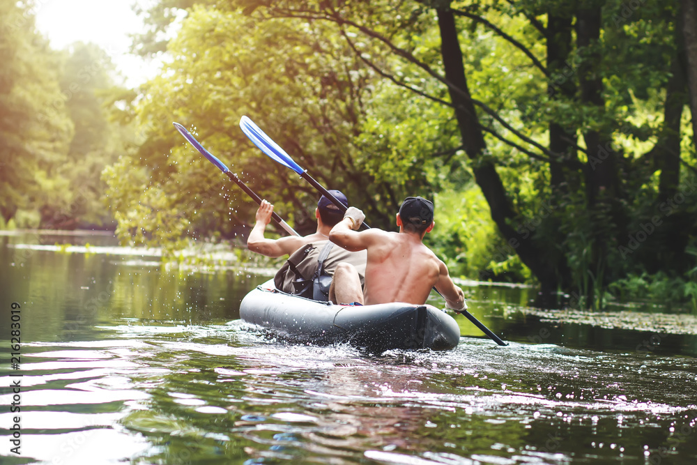 Rafting on the river in a kayak in the summer season. Leisure. Two people in the boat row with oars. Guys sail along the river in a canoe. Adventures of friends in the summer on the river