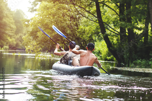 Rafting on the river in a kayak in the summer season. Leisure. Two people in the boat row with oars. Guys sail along the river in a canoe. Adventures of friends in the summer on the river