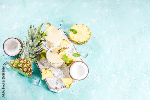 Refreshing summer drink, homemade pina colada cocktail, on a light blue background, with pieces of pineapple, coconut, ice and mint leaves, copy space top view