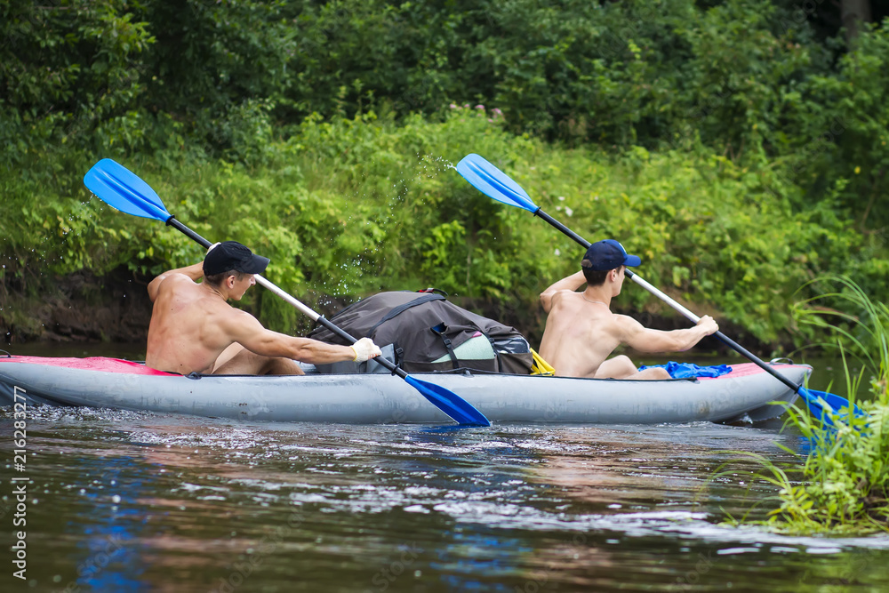 Two young sports guy in a boat rowing oars on the water. Kayaking along the river in the summer season. Rafting on the river in a canoe