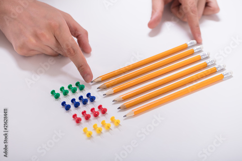 Person's Hand Arranging Pencils And Multi Colored Pushpins photo