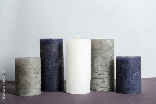 Different decorative wax candles on table against light background