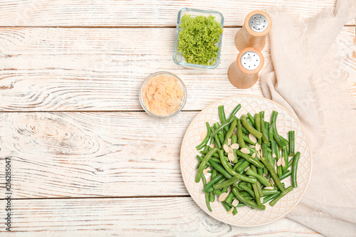 Plate with tasty green beans and almonds on wooden table, top view