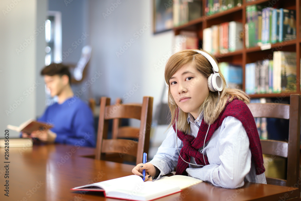 Asian student with headphones studying in library Asian student with headphones studying in library