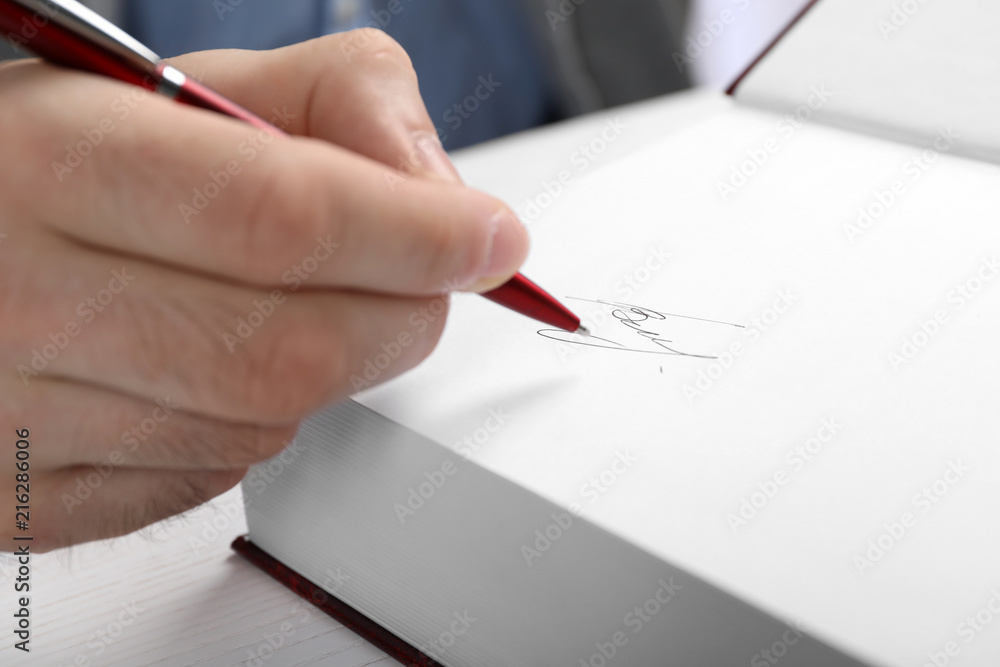 Writer signing autograph in book at table, closeup Writer signing autograph in book at table, closeup
