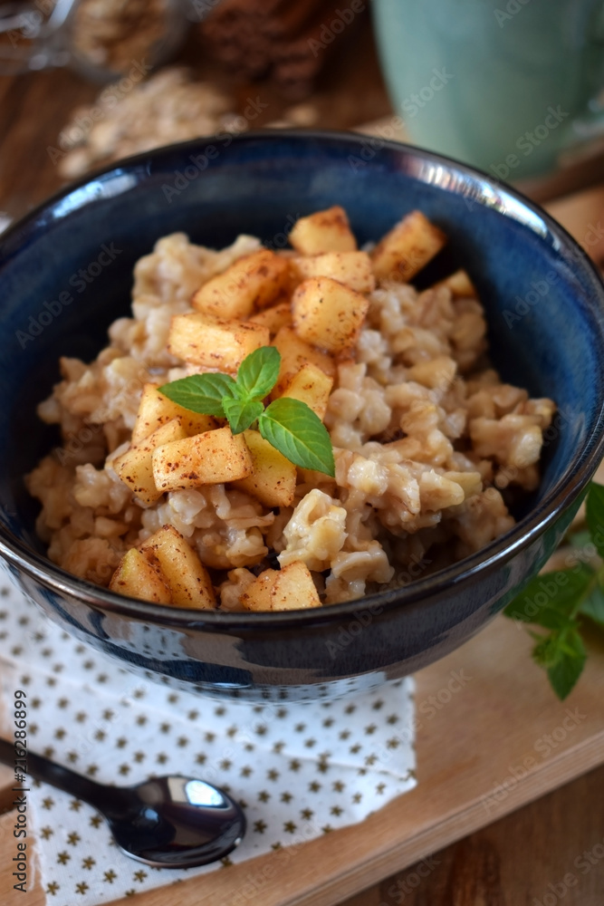 Porridge with apples and cinnamon topped with mint in a blue bowl. British cuisine meal Porridge with apples and cinnamon topped with mint in a blue bowl. British cuisine meal