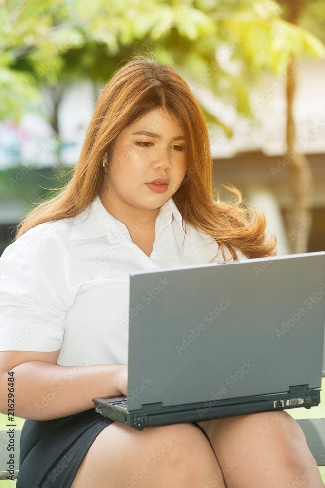 Pretty Asian fat woman pose working with laptop on a chair in the park. Pretty Asian fat woman pose working with laptop on a chair in the park.