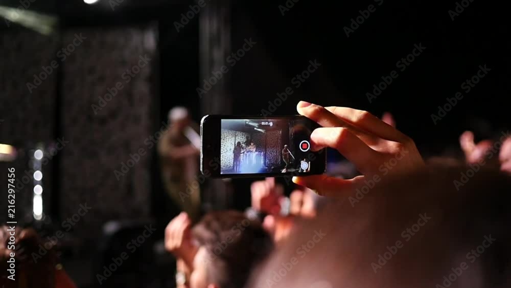Spectator fan shooting video via smart phone at a music concert lumiere