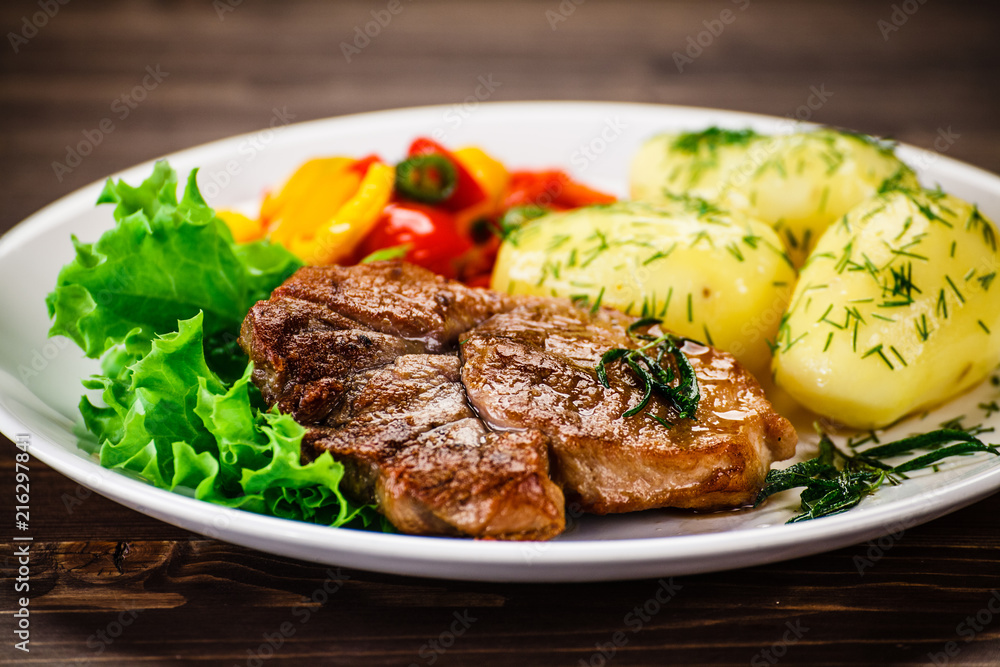 Grilled steak, baked potatoes and vegetable salad on wooden background 