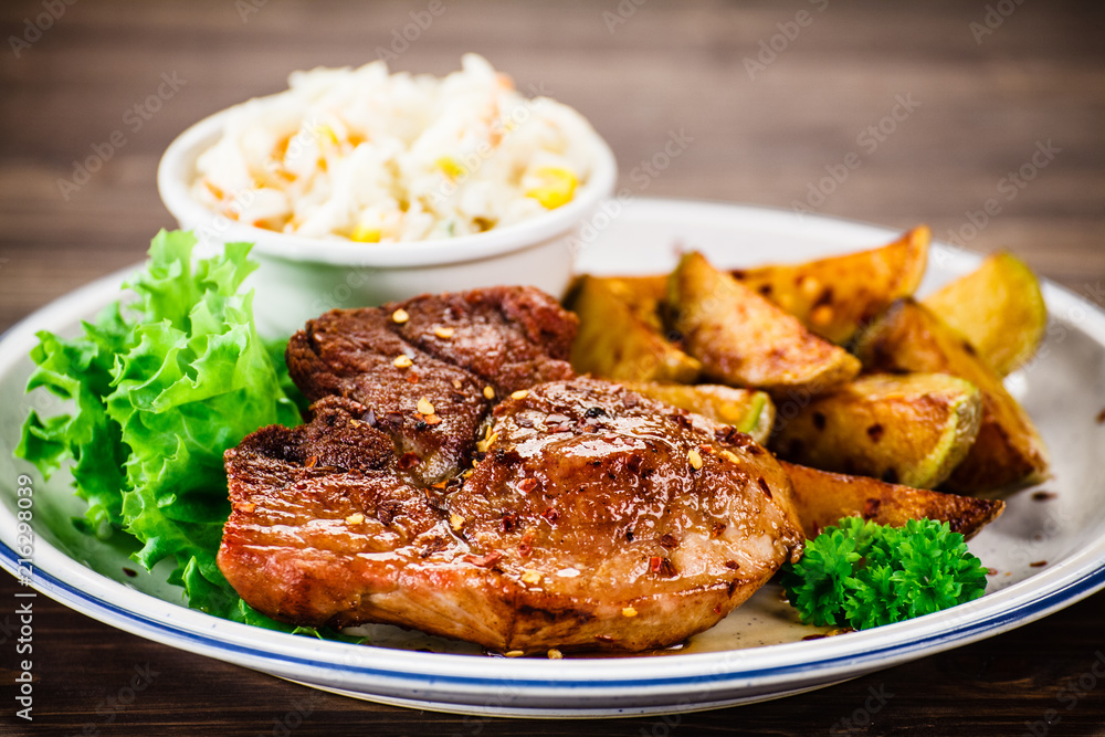 Grilled steak with baked potatoes and vegetables served on wooden table Grilled steak with baked potatoes and vegetables served on wooden table