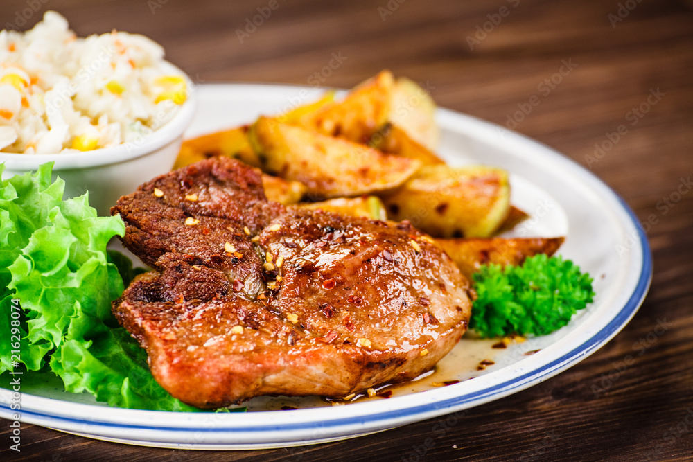 Grilled steak with baked potatoes and vegetables served on wooden table Grilled steak with baked potatoes and vegetables served on wooden table