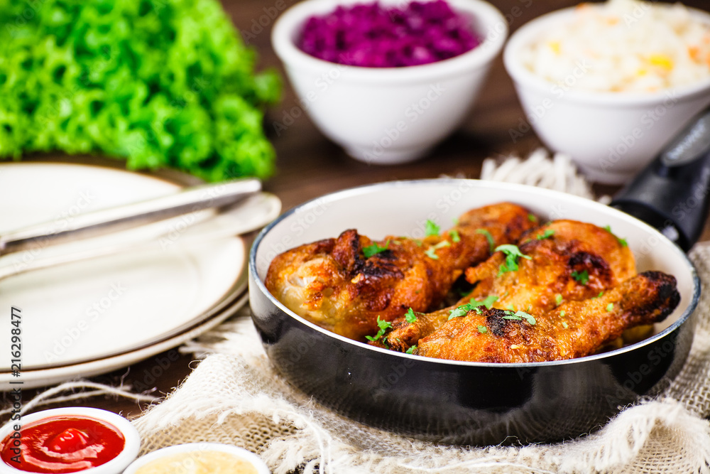 Fried drumsticks in pan with vegetables on wooden table Fried drumsticks in pan with vegetables on wooden table