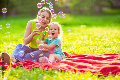 Happy family in park -Female child blows soup foam and make bubbles with her mother in nature.