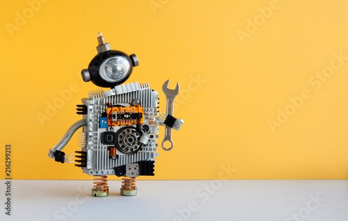 Hand wrench robot serviceman on yellow background. Cyborg toy with lamp bulb head, futuristic silver body. Copy space