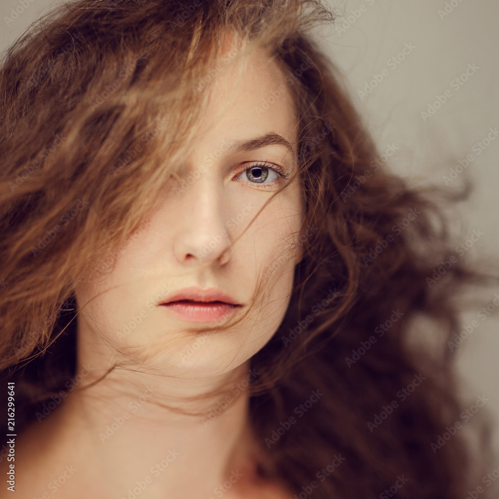 Beautiful young woman with long curly hair and natural make up beauty portrait, looking into camera Beautiful young woman with long curly hair and natural make up beauty portrait, looking into camera